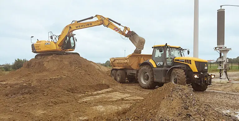 Ein Bagger lädt Mutterboden auf einen Anhänger