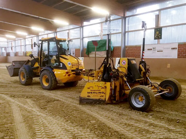 Ein Fahrzeug führt Graderarbeiten in einer Reithalle aus